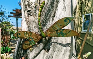 Metal dragon fly and wooden mask on a palm trunk at the 2022 Gate and Garden Tourk